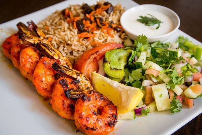 A plate with shrimp skewers, rice and salad.