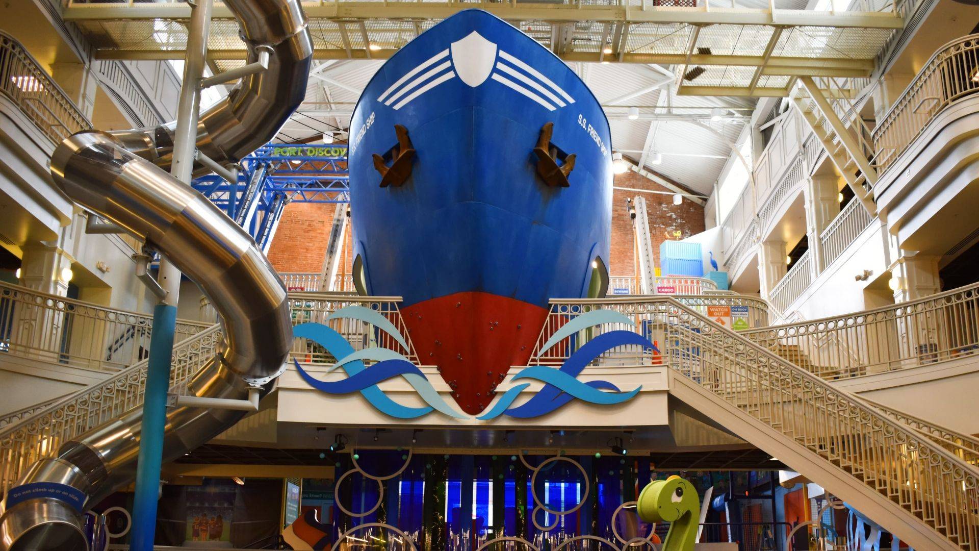 A large blue boat in a building with a slide.