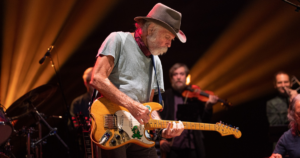 Bob Weir & Wolf Bros playing instruments on stage.in a hat is playing an electric guitar.