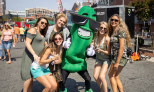 A group of women posing with a pickle mascot.