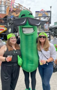Three women posing for a picture with a pickle mascot.