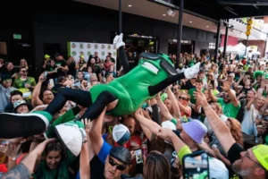 A green mascot is being carried by a crowd of people.