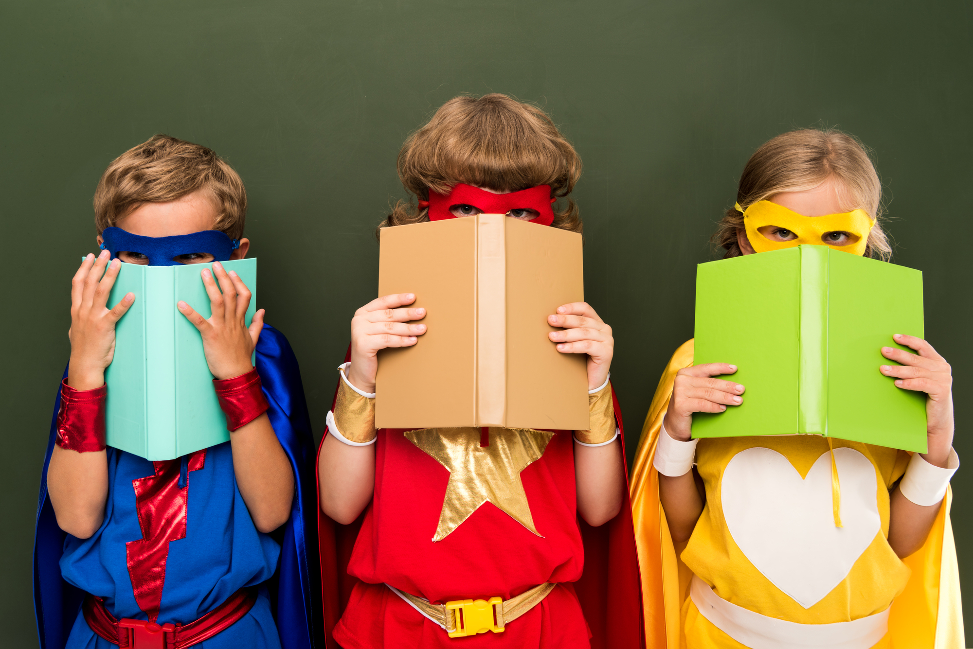 Three children dressed up as superheroes holding books, taking part in November's Fun-Filled Adventures Near Harbor Park Garage!
