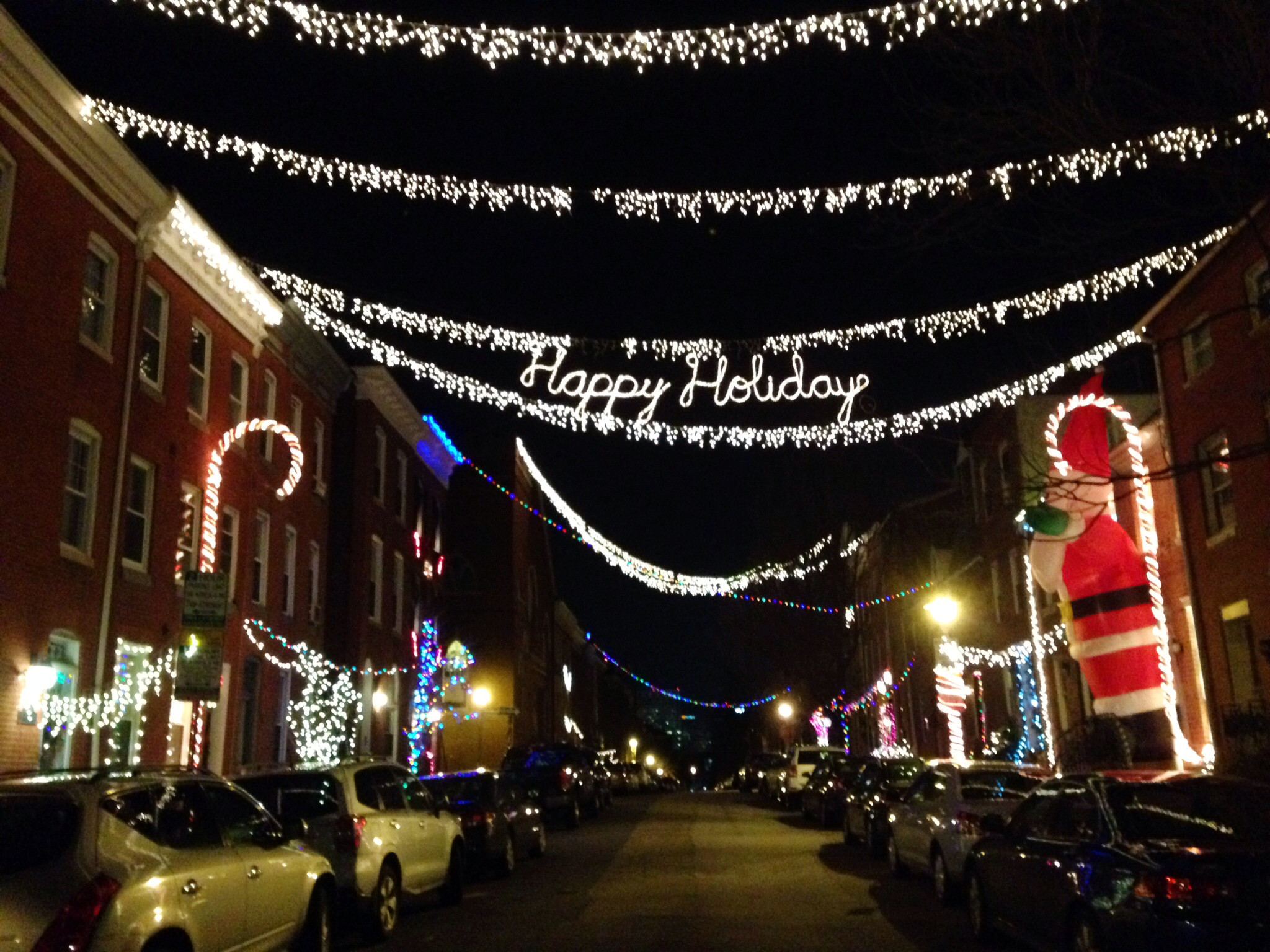 A festive holiday guide to the Christmas lights adorning the charming streets of Federal Hill in Baltimore, where parked cars add to the picturesque scenery.