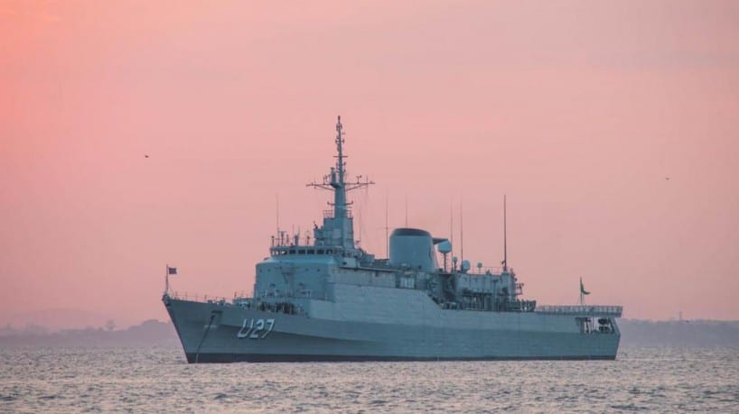 A large navy ship in the water at sunset.