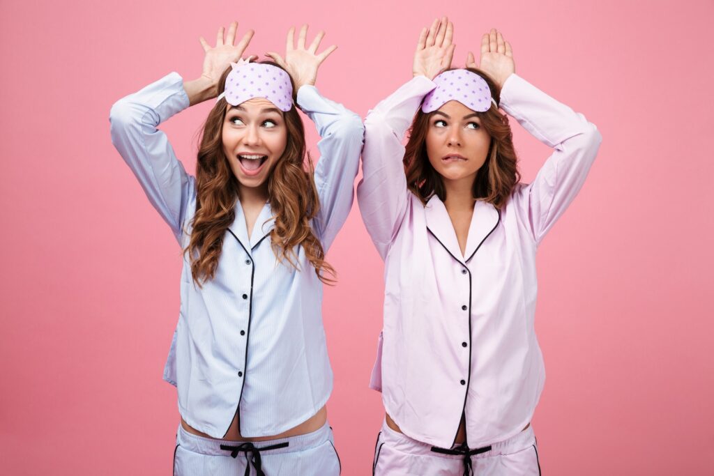 Two young women on a pink background, wearing pajamas.