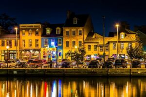 A festive view of Fells Point at night with cars parked by the water.