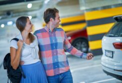 A man and woman walking together in a parking garage, with the man holding a car key and pointing toward a white SUV.