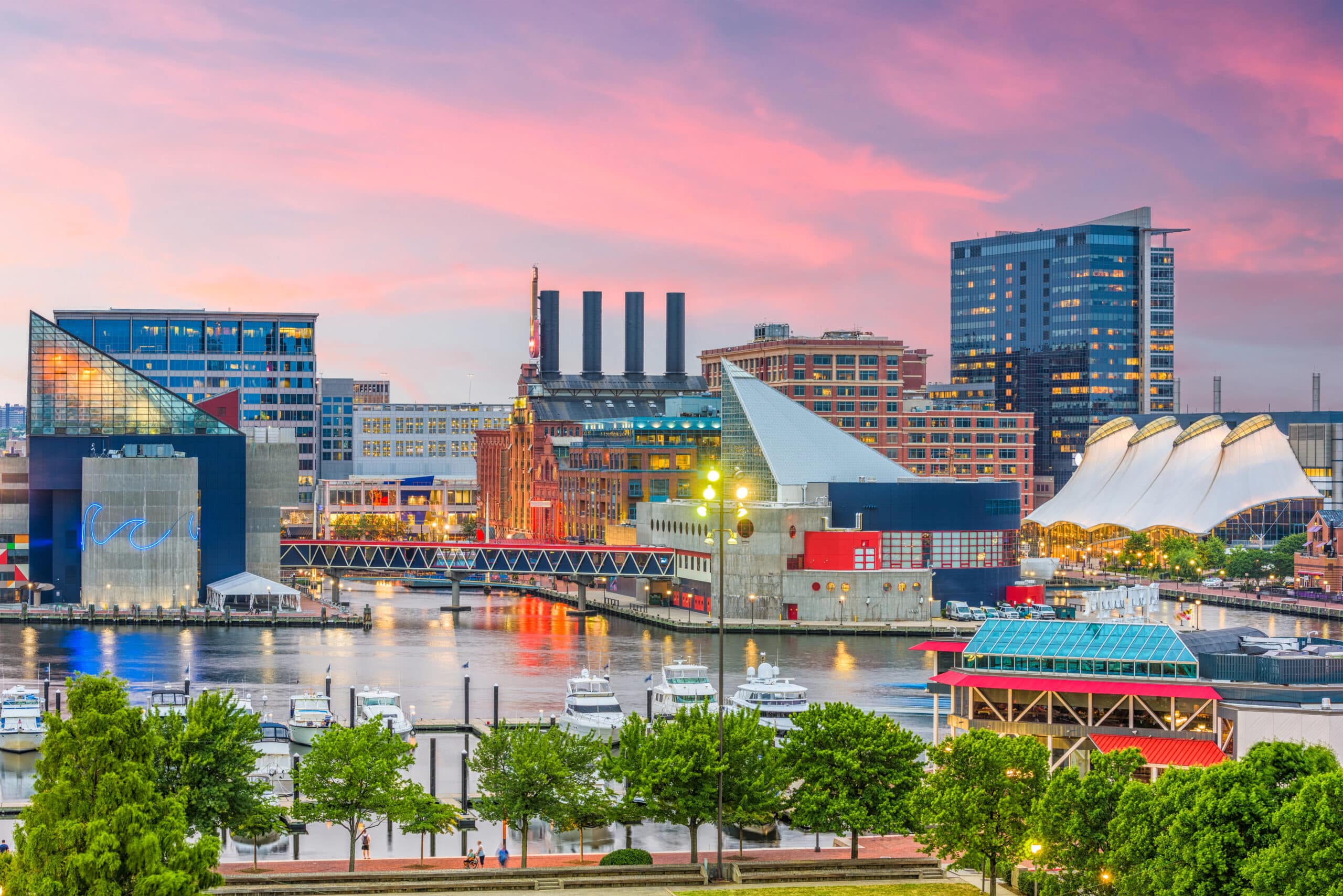 Baltimore Inner Harbor at sunset, featuring modern buildings, the National Aquarium, waterfront, boats, and colorful sky.