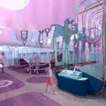 Children and adults interact with various play structures and activity stations in a brightly lit, modern indoor play area with purple and blue decor.