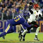 A Cincinnati Bengals quarterback prepares to throw the football as two Baltimore Ravens defenders attempt to tackle him during a game.