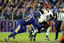A Cincinnati Bengals quarterback prepares to throw the football as two Baltimore Ravens defenders attempt to tackle him during a game.