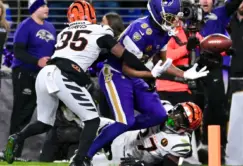 A Baltimore Ravens player attempts to catch a football while being defended by two Cincinnati Bengals players during a game.