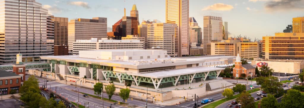 A large modern convention center sits in an urban downtown area surrounded by high-rise buildings and busy streets.