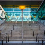 Wide concrete staircase with metal railings leads up to a modern glass Baltimore Convention Center; a single lit streetlamp stands at the center of the steps.