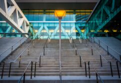 Wide concrete staircase with metal railings leads up to a modern glass Baltimore Convention Center; a single lit streetlamp stands at the center of the steps.