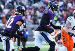 Two Baltimore Ravens football players, Gilman and Van Noy, in purple uniforms run with the ball during a game against the Cincinnati Bengals, whose players wear orange and white uniforms.