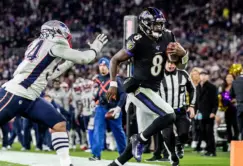 A Baltimore Ravens player runs with the football while being chased by a New England Patriots defender during an NFL game.
